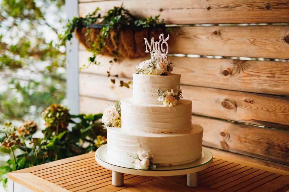 Dreistöckige weiße Hochzeitstorte mit Blumen und „Mr & Mrs“-Topper