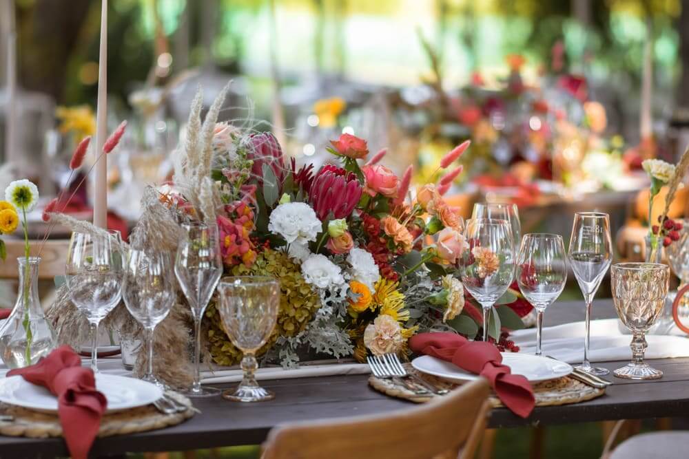 Festlich gedeckte Tafel mit buntem Blumengesteck, Weingläsern und roten Servietten